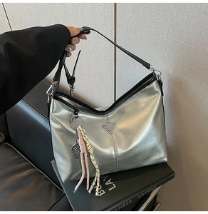 Chic silver tote bag with metallic finish and decorative woven tassel on black strap