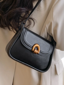 Classic black saddle shoulder bag with golden buckle shown on a beige blazer