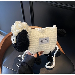 Detail of handmade knit sheep crossbody bag with Faerie Bag label on dark leather background