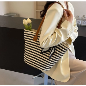 Detail of striped straw tote bag featuring a black and white bow with brown leather handles