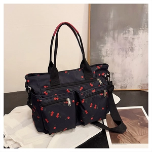 Detail of cherry print tote bag featuring dual front zipper pockets and top handles