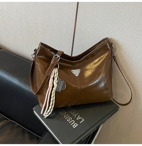 Detail of a brown leather hobo bag with triangle metal buckle and woven charm