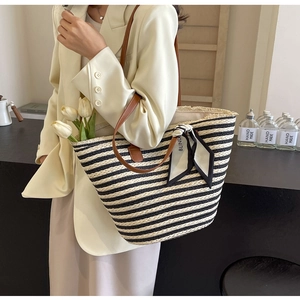 Detail of striped straw tote bag with brown leather handles and decorative scarf