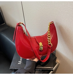 Macro view of red patent leather crescent bag featuring gold metal turn-lock and chain