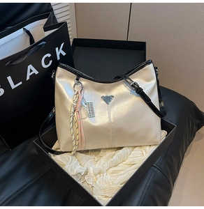 Detail of soft cream faux leather tote with metal triangle and woven tassel in gift box