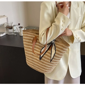 Detail of striped straw tote bag with brown leather handles and printed silk scarf