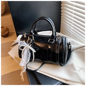 Close-up of black glossy mini bowling bag with delicate white lace bow and pearl chain