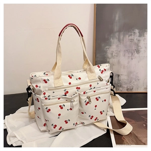 Close-up of white canvas tote with red cherry prints, zipper pockets and side pouch