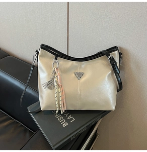 Close-up of cream soft leather tote bag featuring a triangle metal plate and abacus pendant