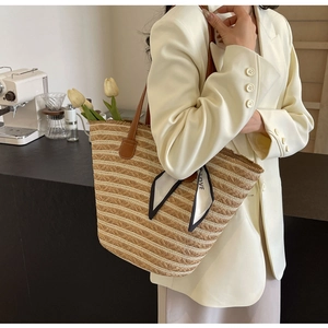 Detailed view of straw woven tote bag with leather handles and decorative silk scarf