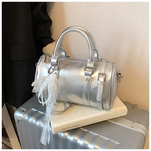 Close-up of silver metallic Boston bag featuring lace bow and pearl charm on a white book