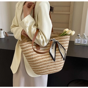 Detailed macro view of woven straw tote bag with leather strap and decorative printed scarf