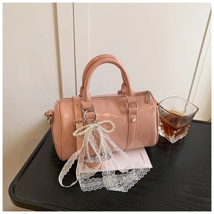 Detail of pink patent leather Boston bag featuring pearl and lace bow charm with gold hardware