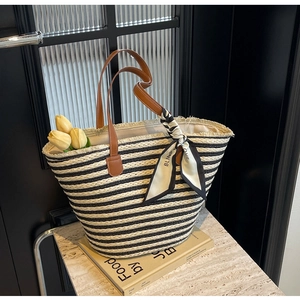 Detail of striped straw tote bag with brown leather handles and decorative silk scarf