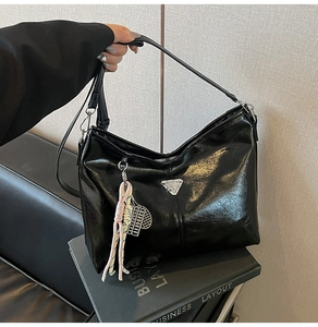 Detail view of a black patent leather tote bag with silver triangle buckle and woven charm
