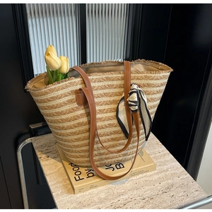Close-up of straw beach tote with leather handles, silk scarf, and yellow tulips on a book