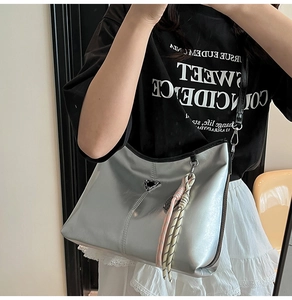 Detail of silver mirror tote bag with triangular metal logo and woven sphere charm
