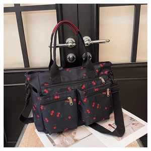 Close-up of black nylon tote with cherry print featuring double front zipper pockets
