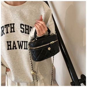 Close-up of quilted black mini vanity bag with golden camellia flower and chain strap