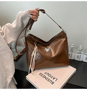 Detail of dark brown glossy leather tote bag with metallic triangle and tennis racket charm