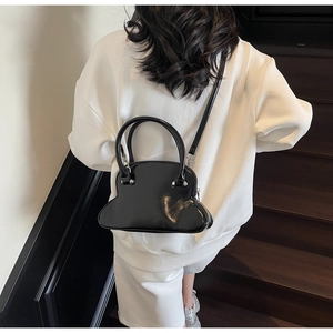 Detail of glossy black toast-shaped handbag featuring unique wavy base and silver hardware