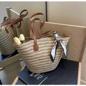 Detail of straw woven tote bag featuring brown leather straps and a decorative silk scarf