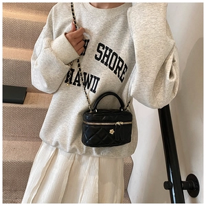 Detail of black quilted mini bag with gold chain strap and flower charm pendant