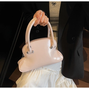 Detail view of pink patent leather shell bag with silver ring handles and sleek zipper