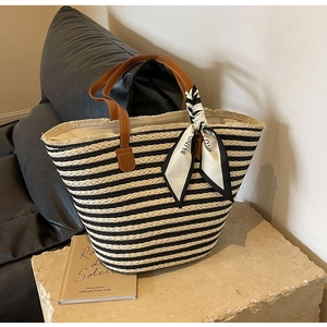 Close-up of striped straw tote bag with brown leather handles and Blind For Love scarf detail