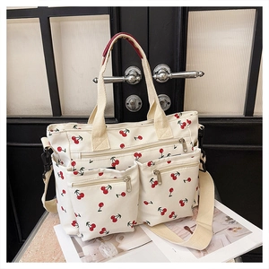Close-up of white canvas tote bag featuring red cherry prints and front zipper pockets