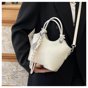Dettaglio di una borsa a secchiello in pelle bianco crema con manico intrecciato e ciondoli