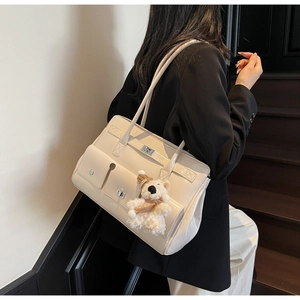 Detailed side view of off-white faux leather tote bag with functional pockets and teddy bear charm