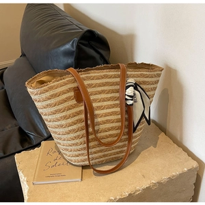 Detail of striped straw tote bag with brown leather straps and decorative printed silk scarf