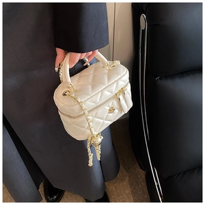 Close-up of beige quilted box bag with camellia clasp and gold ball chain strap detail