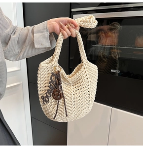Détail d'un sac cabas en maille crème avec un pendentif décoratif en cuir marron