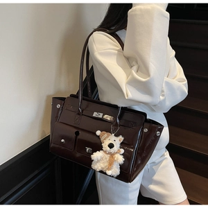 Detail of a dark brown glossy tote bag with silver twist lock and cute bear charm