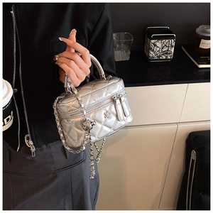 Detail of silver quilted box bag with floral metal pendant and chain strap held by hand