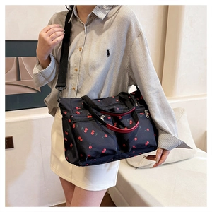 Detail of cherry print canvas tote bag featuring red top handles and multiple zipper pockets
