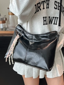 Stylish black glossy leather tote bag with metallic triangle logo and woven pendant charm