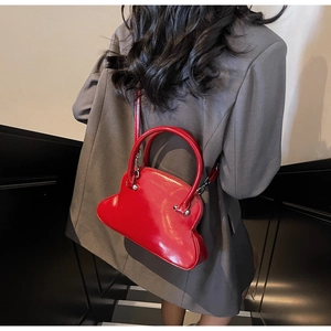 Rear view of a model wearing a shiny red cloud-shaped crossbody bag with grey blazer