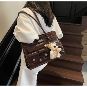 Detail of dark brown patent leather tote with silver lock and a cute plush bear charm