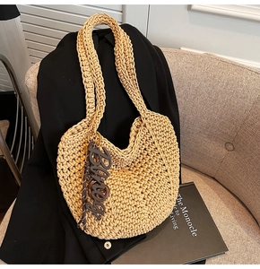 Gros plan du sac cabas beige en maille épaisse avec un pendentif Binog sur un canapé