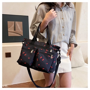 Close-up of black nylon tote bag with cherry print featuring double zippers and strap