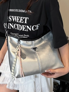 Metallic silver tote bag with triangle logo and tennis racket charm shown as a shoulder bag
