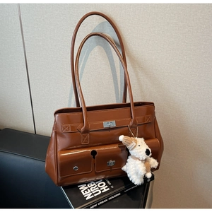 Brown polished leather tote bag with metal lock detail and a plush puppy charm accessory