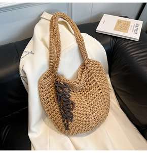 Détail d'un grand sac cabas en maille avec pendentif lettre marron sur blazer blanc