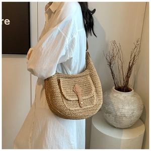 Detailed side view of a straw crescent shoulder bag with leather flap and button accent