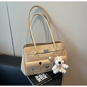Detail view of beige multi-pocket shoulder bag with metal twist locks and plush puppy charm