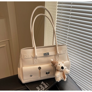 Detail view of off-white tote bag with leather texture, pockets and a cute plush bear charm