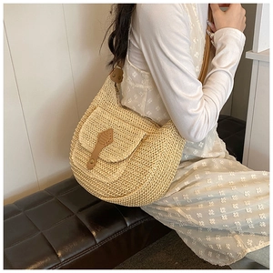 Detail of straw woven hobo bag with brown leather strap worn by a model in a floral dress